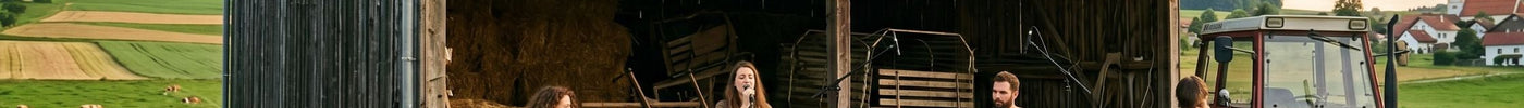 Eine vierköpfige Band bei einer Musikprobe vor einer rustikalen Holzscheune in einer ländlichen Idylle mit einem Traktor, weiten Feldern und einem kleinen Dorf im Hintergrund.