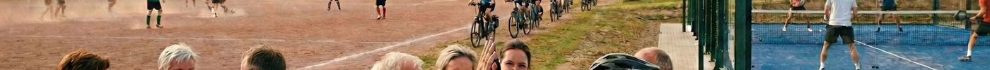 Menschen aus dem Dorf genießen den Sport und Essen. Man sieht viele Teilnehmer beim Sportfest 2026. Menschen fahren Fahrrad, spielen Fußball und Paddel. Die anderen speisen und lachen.