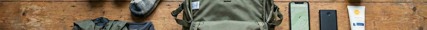 Auf diesem Bild sieht man die ultimative Packliste für eine Wanderung. Rucksack, Socken, Jacke, Proviant, Erstehilfeset, Handy, Sonnencreme und Sonnenbrille.