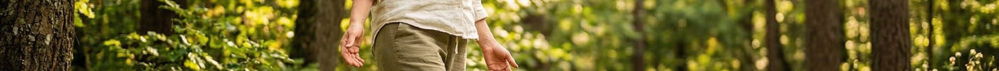 Eine Frau steht barfuß im Wald und lässt die Sonne auf sich strahlen.