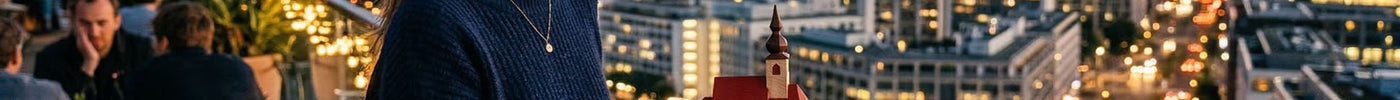 Eine Frau steht auf dem Balkon einer Bar und schaut in die Ferne. Sie hält dabei eine kleine Kirche in der Hand.