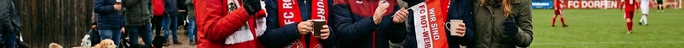 Fünf jubelnde Frauen in rot-weißer FC Rot-Weiss-Fankleidung am Spielfeldrand eines Fußballvereins.