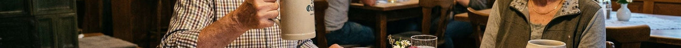 Ein älteres Ehepaar genießt ein traditionelles Abendessen - Schnitzel, Brotzeit - in einem gemütlichen, rustikalen Gasthaus. Der Mann erhebt seinen Bierkrug.