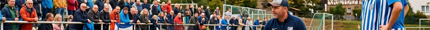 Ein Fußballtrainer erklärt seiner Jugendmannschaft in blau-weiß gestreiften Trikots in der Halbzeitpause Taktiken auf dem Spielfeld. Im Hintergrund stehen Zuschauer vor einer Kulisse aus Fachwerkhäusern und einer Kirche.