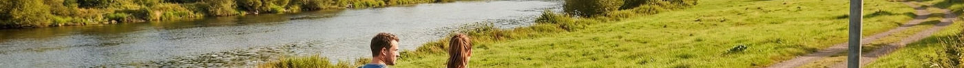 Auf dem Bild sieht man zwei Wanderer. Eine Frau, einen Mann und einen Hund, die gemeinsam an der Lahn wandern gehen.