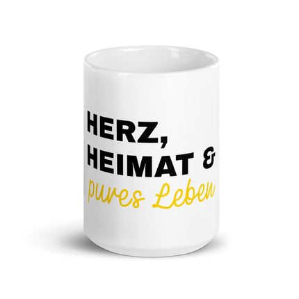 Eine weiße Tasse mit der Aufschrift Herz, Heimat & pures Leben.