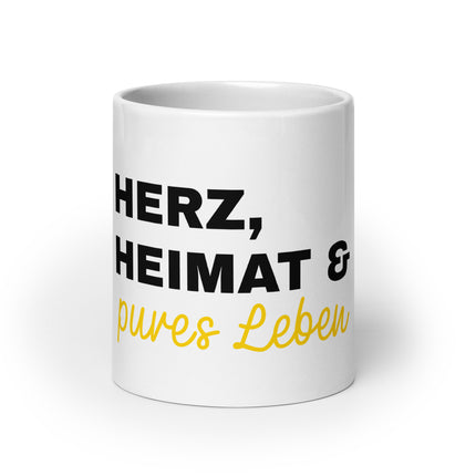 Eine weiße Tasse mit der Aufschrift Herz, Heimat & pures Leben.