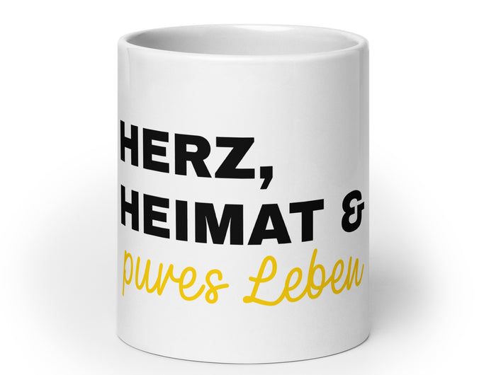 Eine weiße Tasse mit der Aufschrift Herz, Heimat & pures Leben.